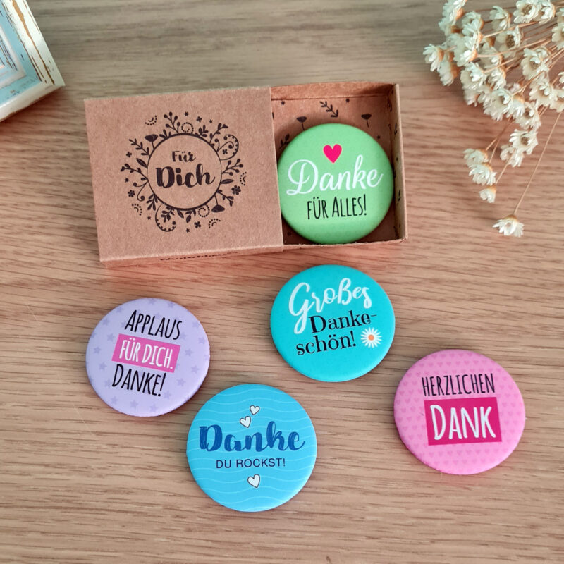 Geschenke für Mitarbeiter: Bunte Buttons mit 'Danke'-Botschaften und einer dekorativen Box mit Aufschrift 'Für Dich